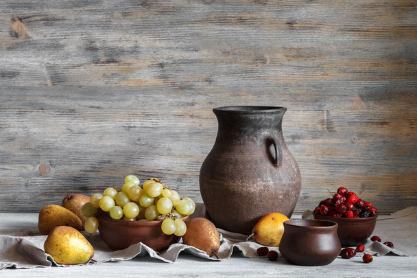 素朴なスタイルでまだ生活:木製のテーブルの上に粘土料理、ブドウや梨のセット。窓からの自然光. - 写真・画像