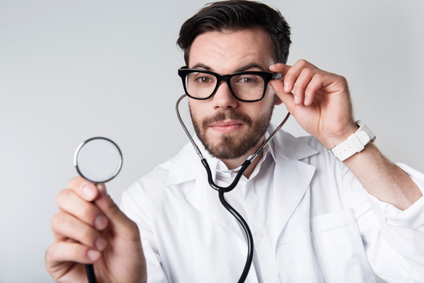Concentrated bearded man holding stethoscope. - Foto, afbeelding