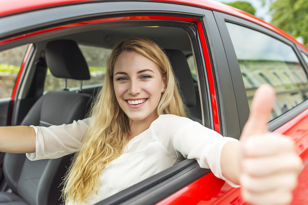 Happy smiling girl in a red car. - Zdjęcie, obraz