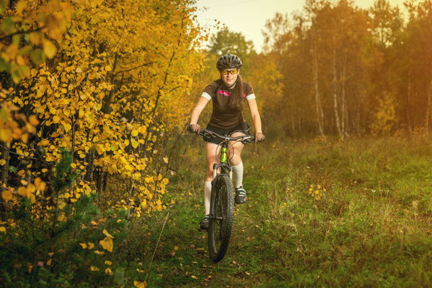 Femme faisant du vélo dans la forêt jaune d'automne sur une prairie
 - Photo, image