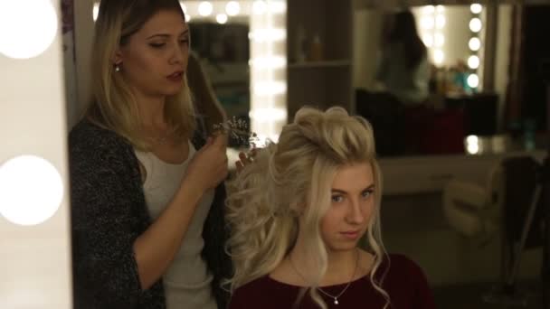 A professional hairdresser does the girl hairstyle , blonde girl - Materiaali, video
