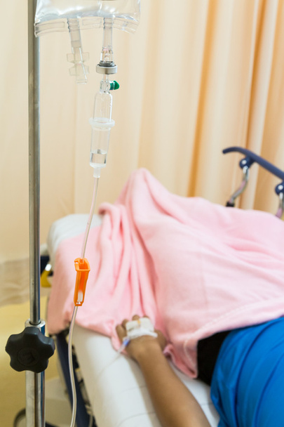Fokus auf intravenöse IV-Tropfen mit Patient im Hintergrund - Foto, Bild