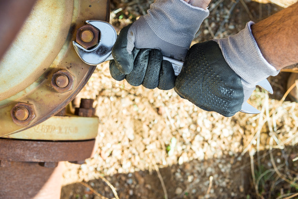 Hände mit Arbeitshandschuhen, die einen Schraubenschlüssel halten und sehr rostige Schrauben festziehen - Foto, Bild