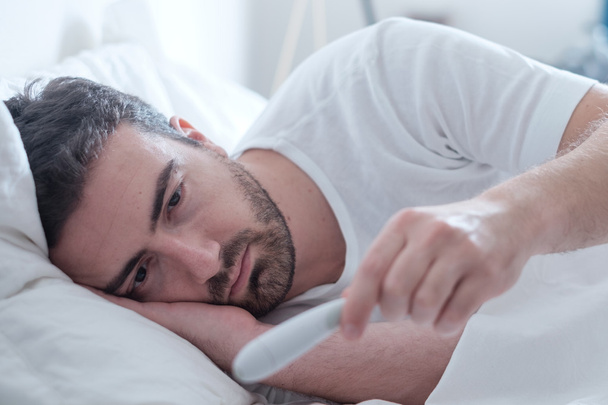 Homme se sentant mal couché dans le lit et regardant le thermomètre
 - Photo, image