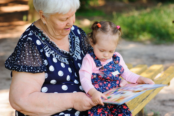 Бабуся і онука читають книгу в парку
 - Фото, зображення