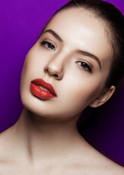Όμορφη γυναίκα με μακιγιάζ με κόκκινα χείλη σε μοβ φόντο - Φωτογραφία, εικόνα