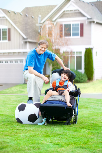 Padre che gioca a calcio con il figlio disabile in sedia a rotelle al parco
 - Foto, immagini