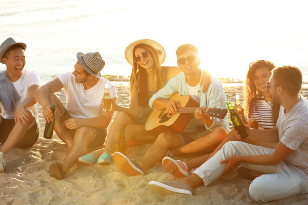 Gruppo di amici che ascoltano chitarra e bevono birra in spiaggia
 - Foto, immagini