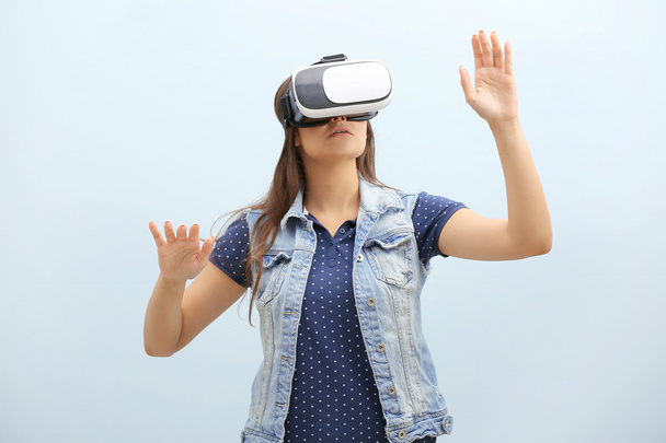 Young woman wearing virtual reality glasses on light background - Foto, imagen