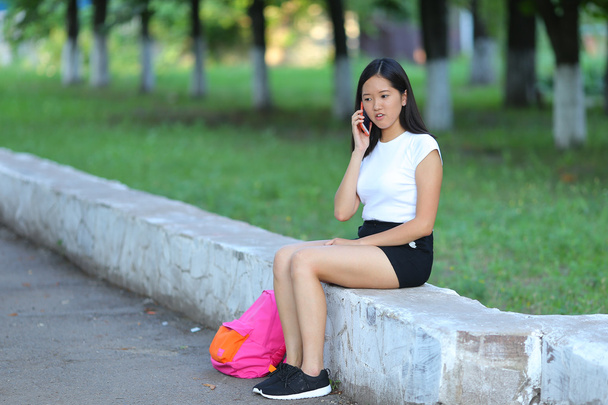 Jong meisje zitten en praten over de telefoon in het park - Foto, afbeelding