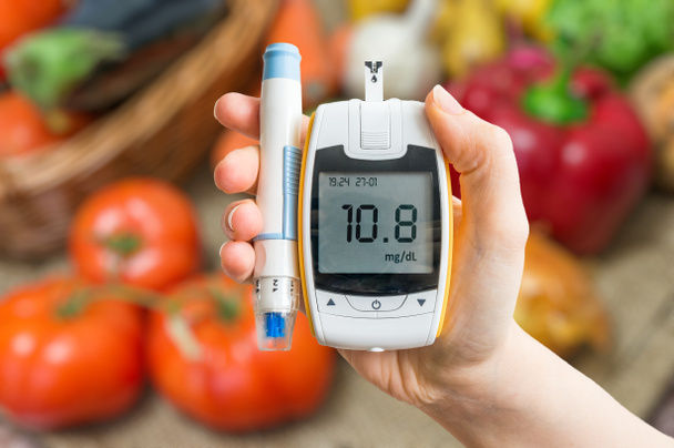 Diabetikus étrend és az egészséges táplálkozás fogalmát. A glukométer és zöldség a háttérben. - Fotó, kép