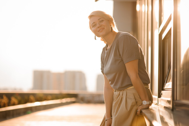 beautiful blonde girl stand against city view in sunny rays at sunset in summer . - Foto, Bild