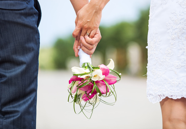 Closeup view of married couple holding hands and carrying bride's bouquet - Photo, Image