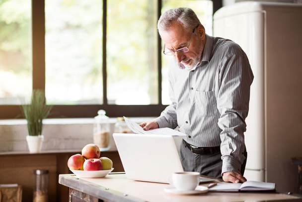 Senior man checking his papers in kitchen at home - Foto, Bild