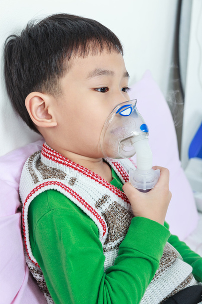 Niño asiático sostiene un inhalador de vapor máscara para el tratamiento del asma
.  - Foto, Imagen