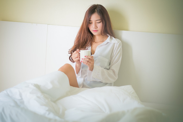 Beautiful brunette woman drinking and morning coffee in bedroom - Фото, изображение