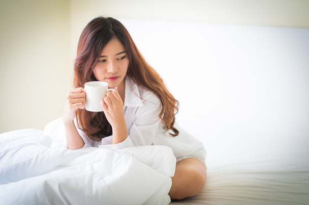 Beautiful brunette woman drinking and morning coffee in bedroom - Fotografie, Obrázek