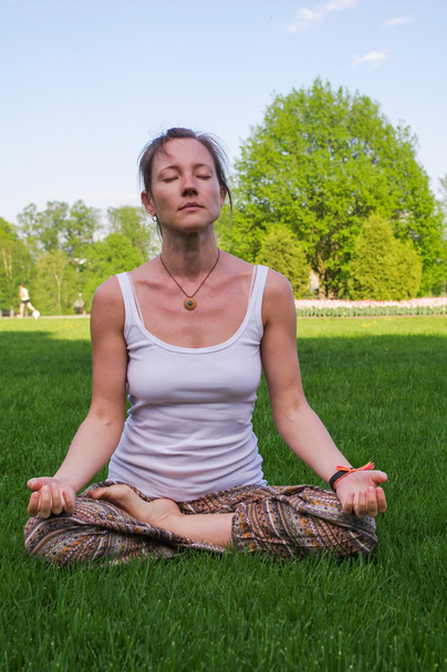 Nuori nainen istuu joogassa aiheuttaa meditaatiota ulkona
 - Valokuva, kuva