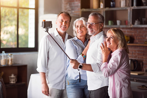Счастливая взрослая семья делает селфи со смартфоном на кухне
 - Фото, изображение