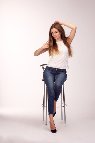 Single happy young woman sitting on a white chair in studio - Foto, immagini
