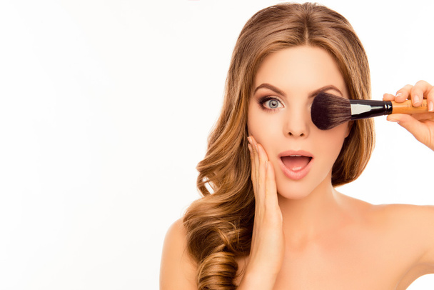Portrait of shocked girl holding makeup brush near eye - Foto, immagini