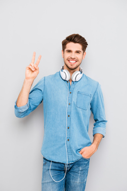 Cheerful guy with white headphones showing two fingers - Фото, зображення