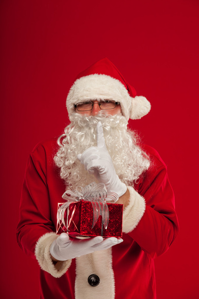 Photo of kind Santa Claus giving xmas present and looking at cam - 写真・画像