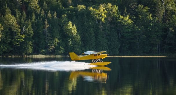 Piccolo aeroplano giallo sui pontoni decolla da un lago dell'Ontario orientale in una serata estiva
. - Foto, immagini