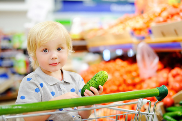 Toddler boy sitting in the shopping cart in a food store or a supermarket - Photo, Image
