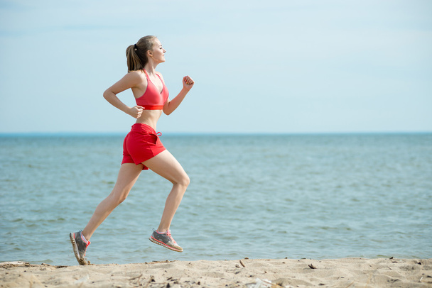 Young lady running at the sunny summer sand beach. Workout.  Jog - Foto, afbeelding
