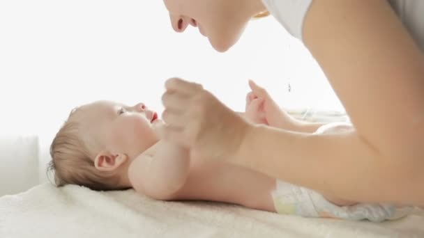 Kaunis nuori äiti suudella häntä 3 kuukautta vanha vauva poika makaa hoitopöydällä edessä iso ikkuna
 - Materiaali, video