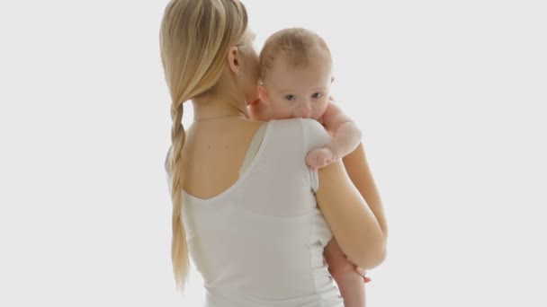 Beautiful young woman hugging her 3 years old baby boy in front of big window. People on white isolated background - Footage, Video