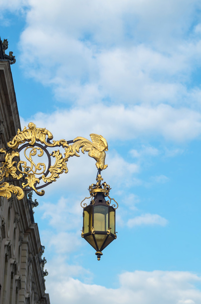 Krásné zlaté ozdobné kované Lucerna (venkovní lampa) visí před historickou budovou na zdi - Fotografie, Obrázek
