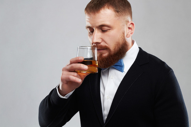 Κοντινό πλάνο ενός κομψού όμορφου γενειοφόρου άνδρα που απολαμβάνει ένα μπράντι ή ουίσκι - Φωτογραφία, εικόνα