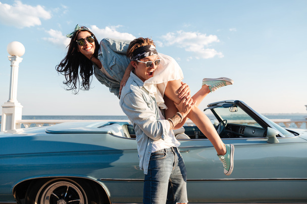 Man carrying his woman and having fun near vintage cabriolet - Photo, image