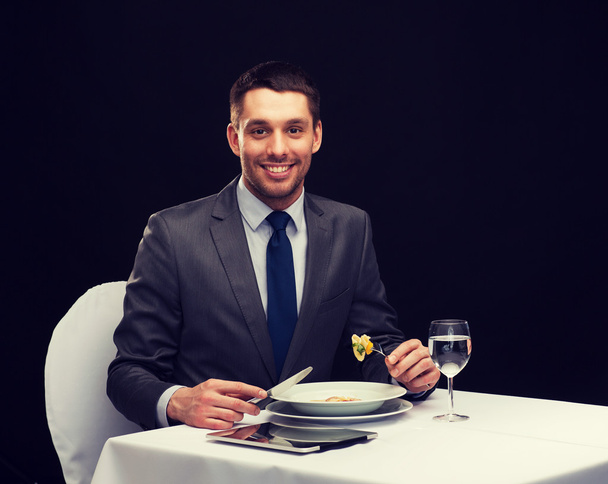 smiling man with tablet pc eating main course - 写真・画像