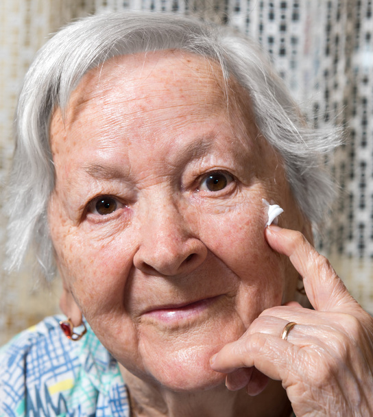 Mujer vieja aplicando crema antienvejecimiento
 - Foto, imagen