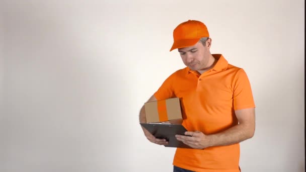 Courier in orange uniform delivering a parcel. Grey backround, isolated. 4K shot - Materiał filmowy, wideo