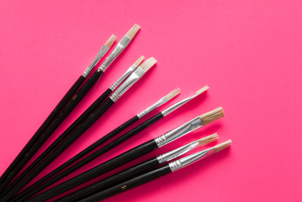 Artists brushes and pens displayed on isolated pink background - Foto, afbeelding