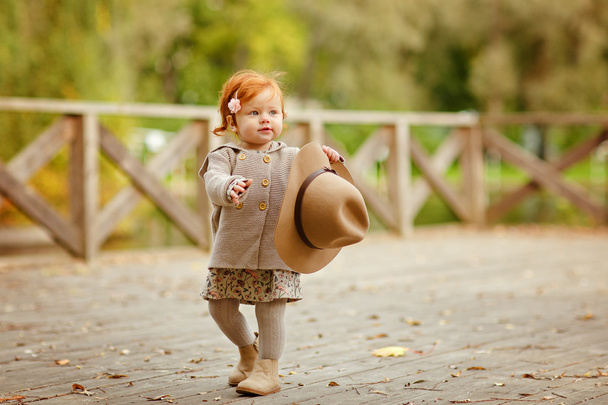 Red-haired baby girl in a hat smiling outdoors in autumn - Fotoğraf, Görsel
