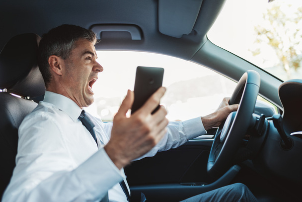 Businessman using his smartphone while driving and having a car accident - 写真・画像