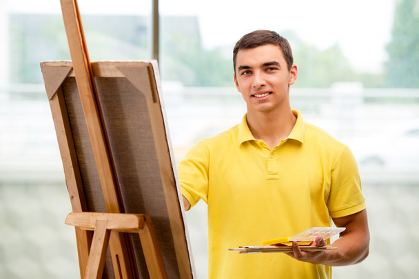 Νεαρός αρσενικός καλλιτέχνης ζωγραφίζει σε φωτεινό στούντιο - Φωτογραφία, εικόνα