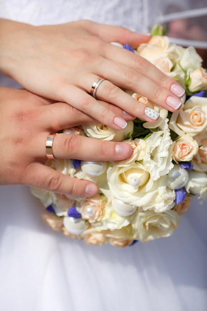 Закройте руки жениха и невесты со свадебным букетом и золотом
 - Фото, изображение