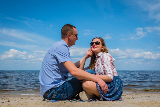um casal amoroso sentado na praia, perto da água, brincando uns com os outros, céu azul no fundo, dia ensolarado, ângulo largo, camas brancas longas
 - Foto, Imagem