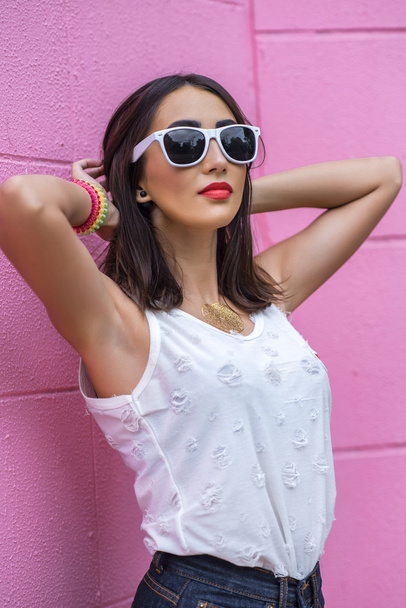 Girl brunette in a park in the summer resting white blouse on  pink background wall, fashion lifestyle. Sensual make-up, tanned skin and bright red lipstick. Portrait of  woman. In sunglasses - Zdjęcie, obraz