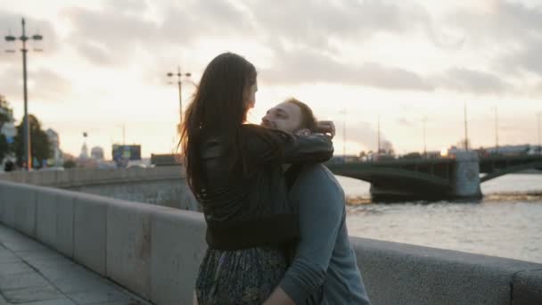 A couple in love swirling around, smiling, kissing at the sunset. Bridge, river at the background, slow mo - Кадры, видео