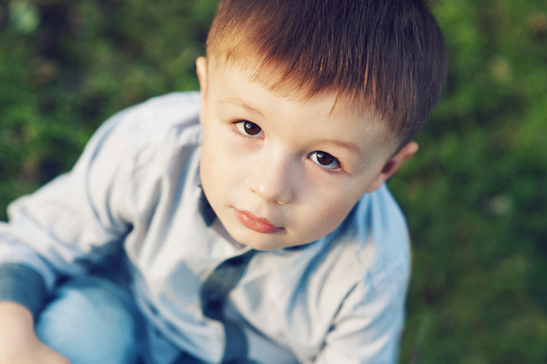 kisfiú ül a fűben kint a parkban - Fotó, kép