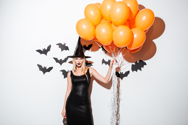 Sexy young woman in witch halloween costume holding orange balloons - Fotoğraf, Görsel