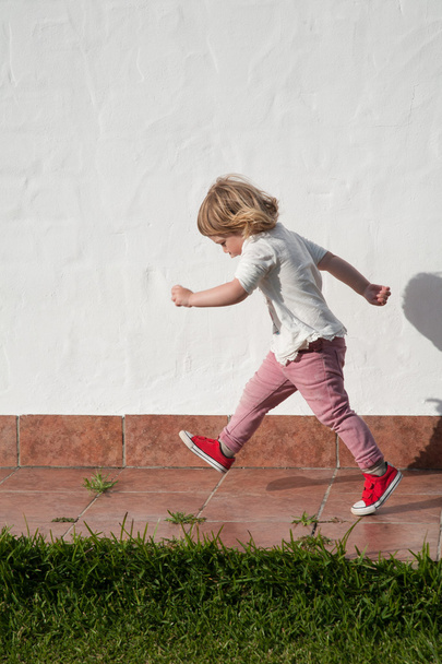 chodící malé dítě v zahradě nad bílou zeď - Fotografie, Obrázek