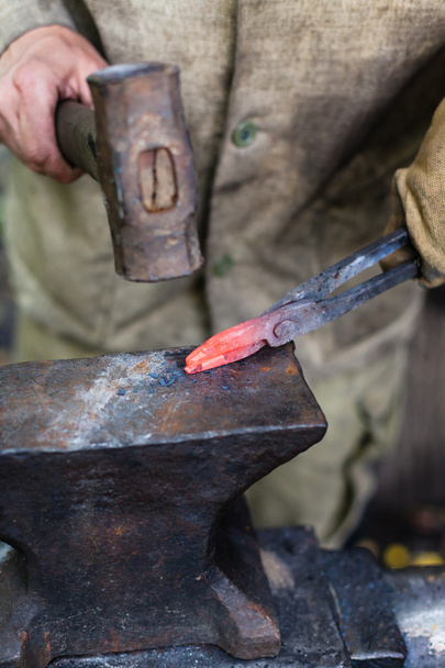Herrero forja pinzas con martillo en yunque
 - Foto, imagen